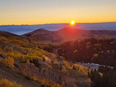 Golden sunset over rolling hills and forest, warm autumn colors, sun kissing the ridge, tranquil valley below.