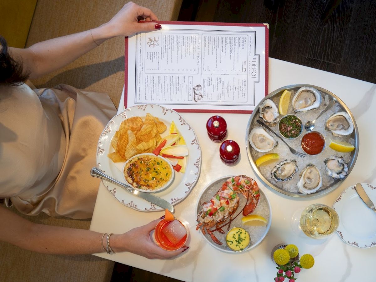 A person sits at a table with a small Santander of oysters on a tray, a plate of chips and a deviled egg, a drink, and a menu on the table.