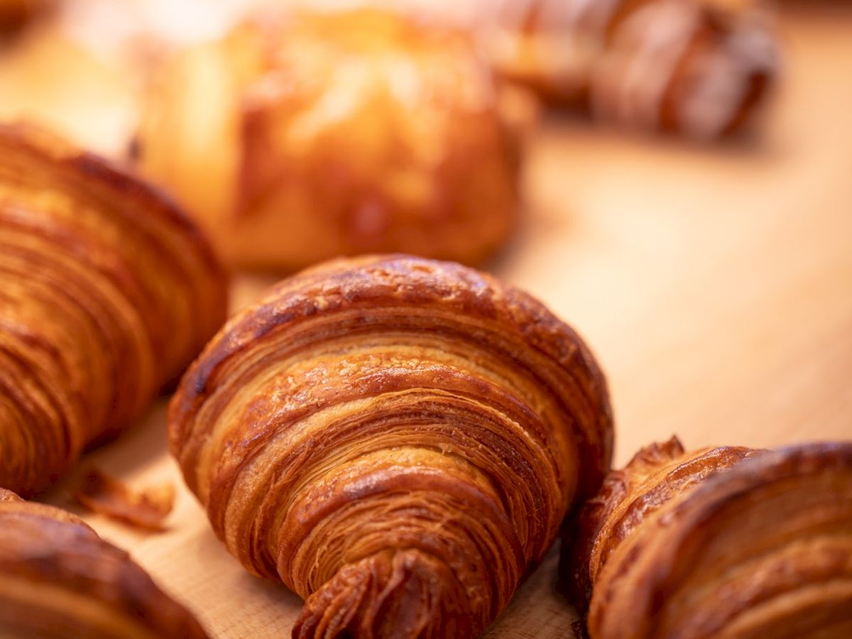 Fresh, flaky croissants with golden-brown, layered pastry on a tray, some blur in the background. Great for breakfast or pastries.