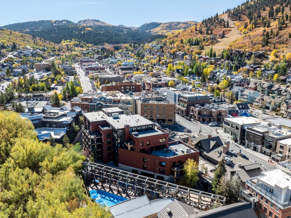 An aerial view of a mountain town with rows of buildings, roads, trees in fall color, and hills stretching into the distance.