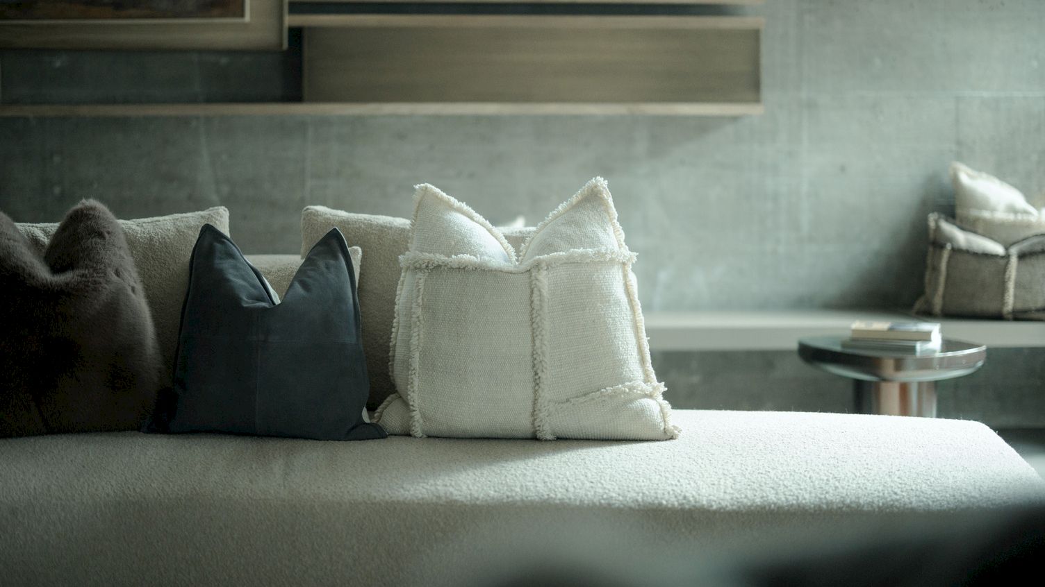 A living-room sofa with dark and white throw pillows, a small glass coffee table, and window light in the background.