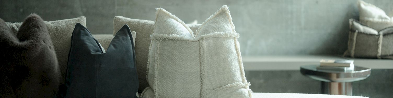 A living-room sofa with dark and white throw pillows, a small glass coffee table, and window light in the background.