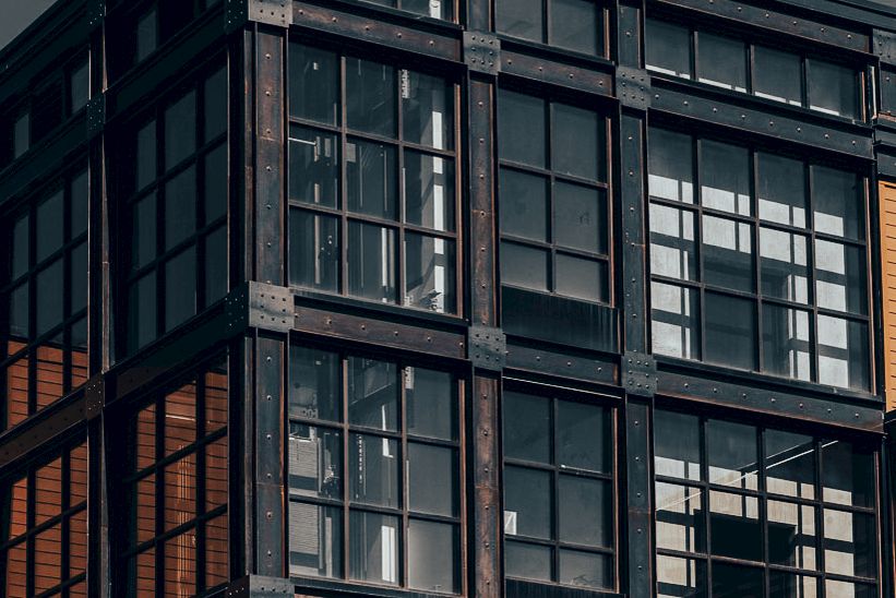 A close-up of a weathered steel-framed building facade with multiple glass windows, lit by warm sunlight.