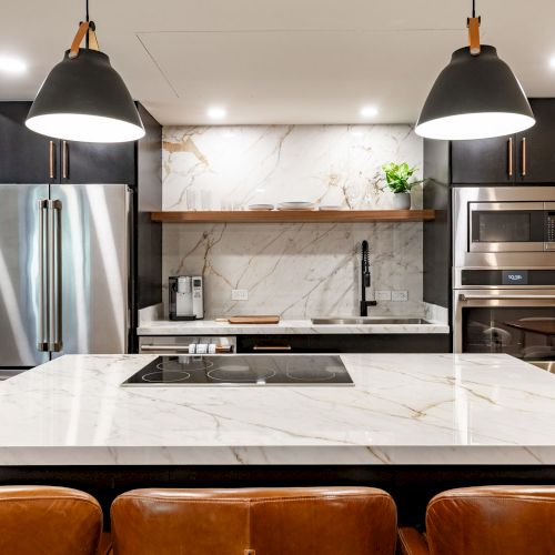 Modern kitchen with marble backsplash and countertop, stainless appliances, and pendant lights over an island, with seating.