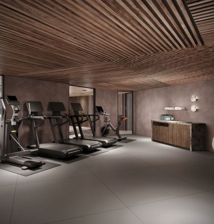 Modern gym with treadmills and exercise bikes under a slatted wooden ceiling; mirrors, benches, and a reception counter are visible.