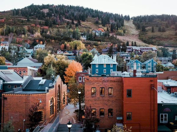 A hillside town with colorful autumn trees and rooftops, brick buildings in front, and a quiet road winding through the valley.